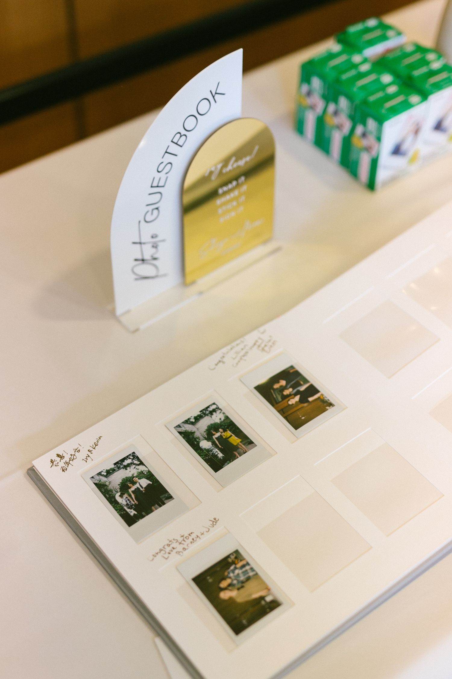 Wedding photo guestbook open on table displaying Polaroid photos beside Fujifilm instax film boxes.
