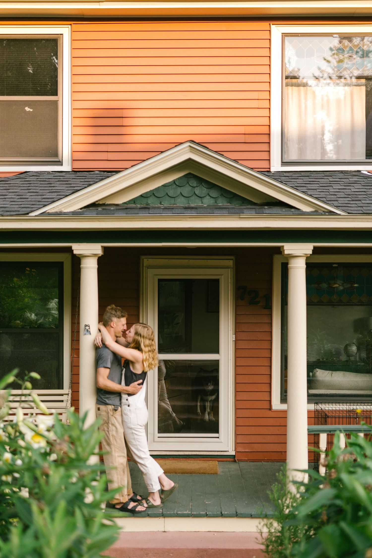 Couple embracing on the porch of an orange craftsman style house.