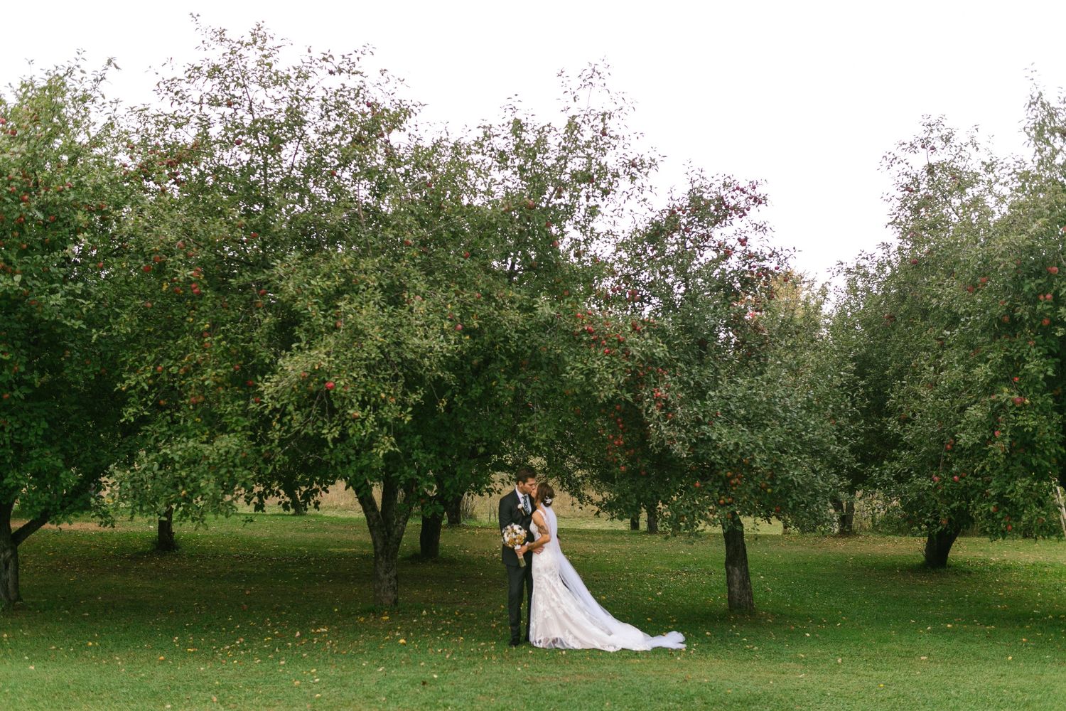 A romantic outdoor wedding scene in an orchard with trees providing a beautiful natural backdrop for the couple.