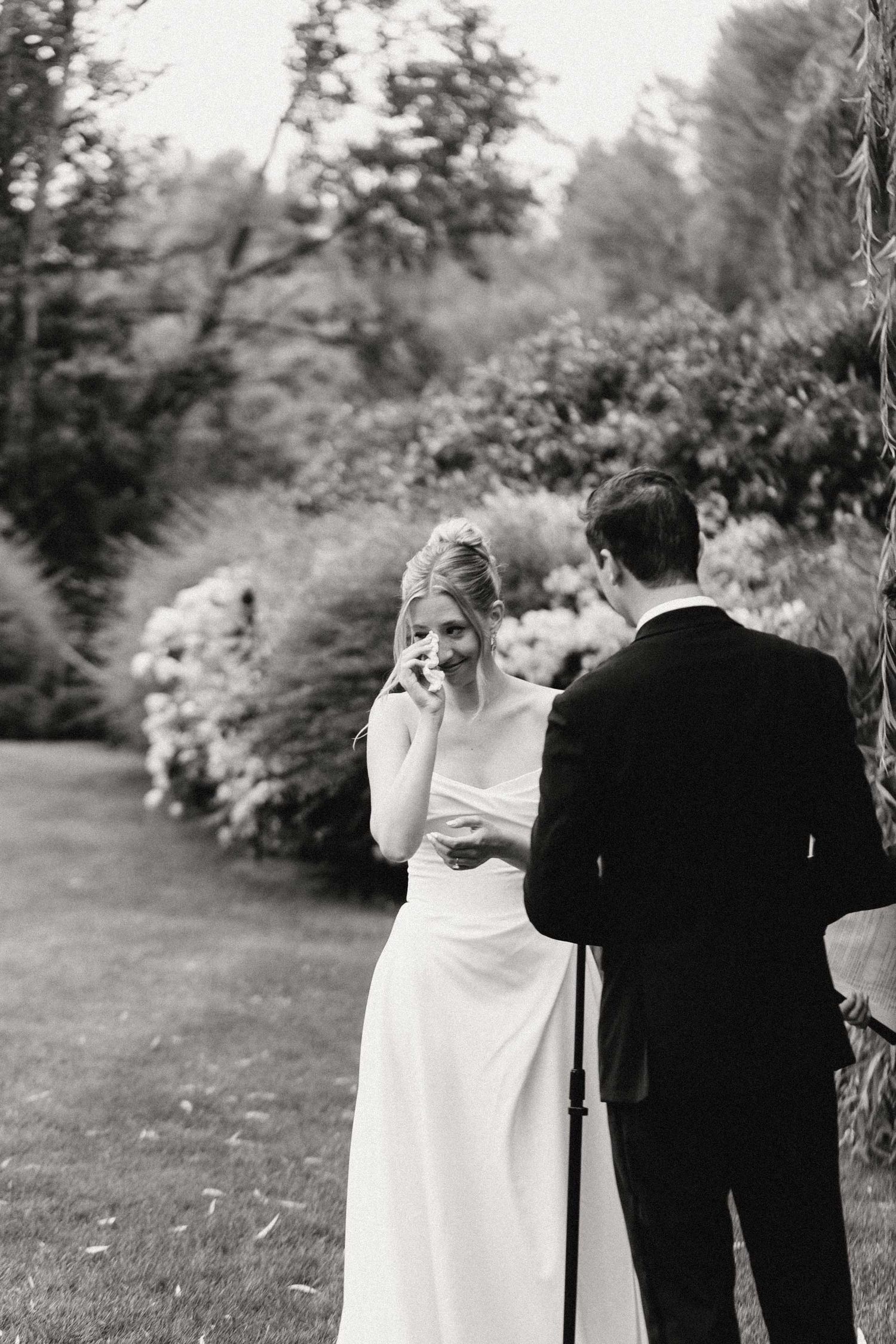 A couple shares a tender moment in a garden setting during their wedding day, surrounded by lush greenery and flowers.