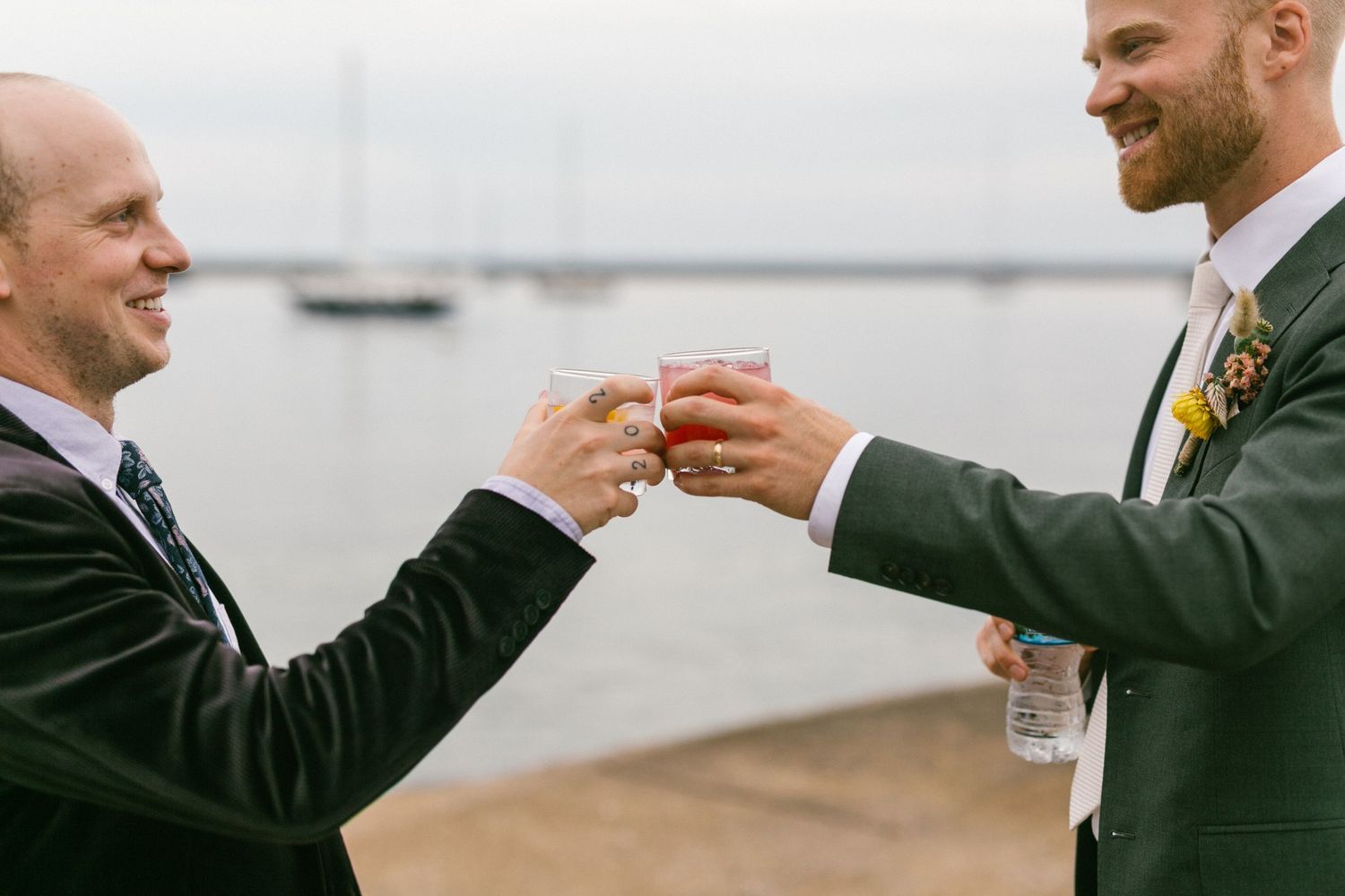 Groomsmen in dark suits share drinks and laughs during a wedding celebration.