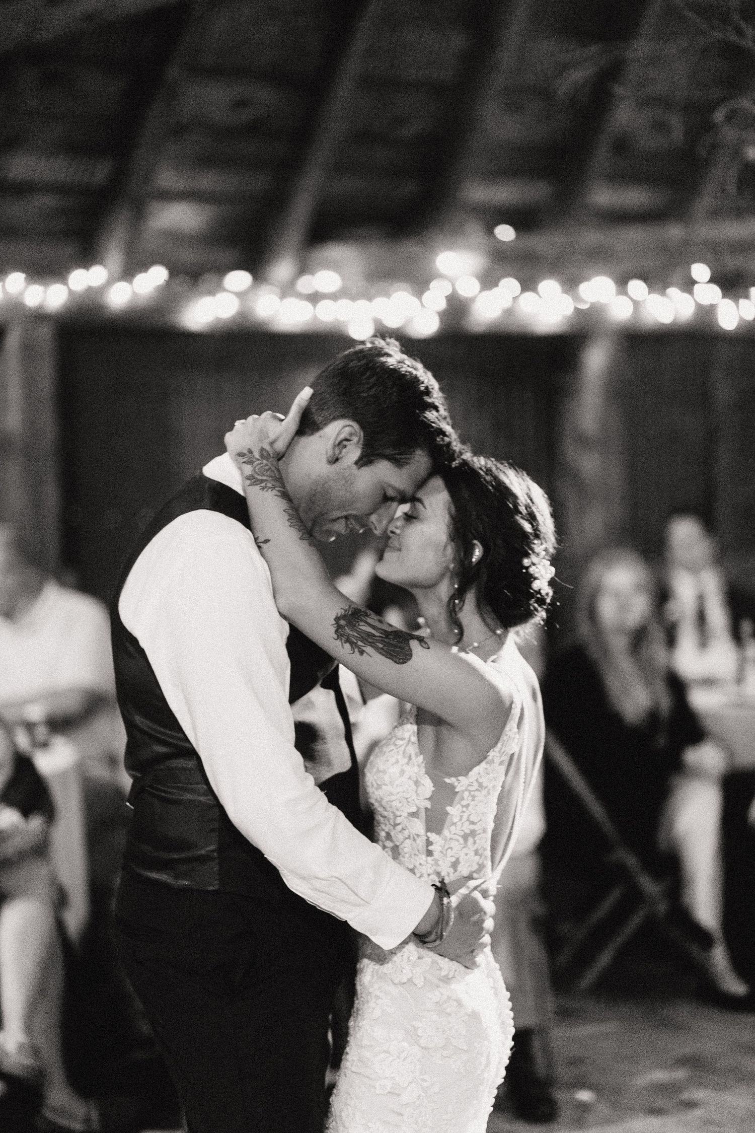 A romantic black and white photo of newlyweds sharing an intimate moment under twinkling lights.