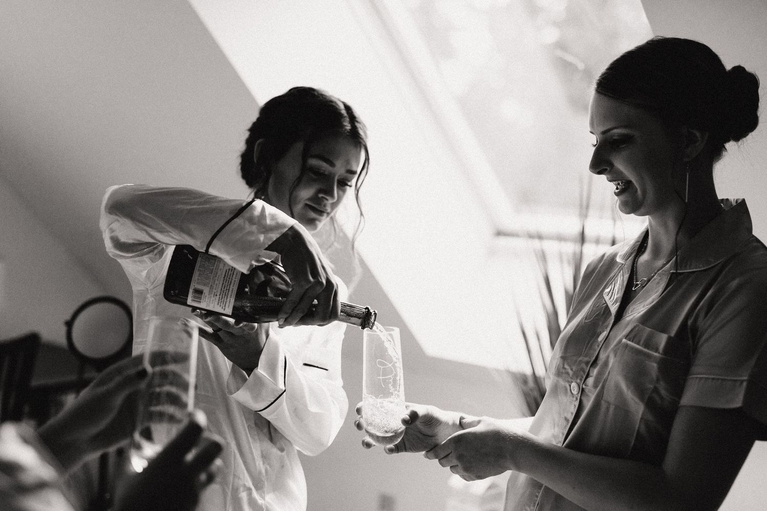 Two people pour and share wine together in a black and white candid moment.