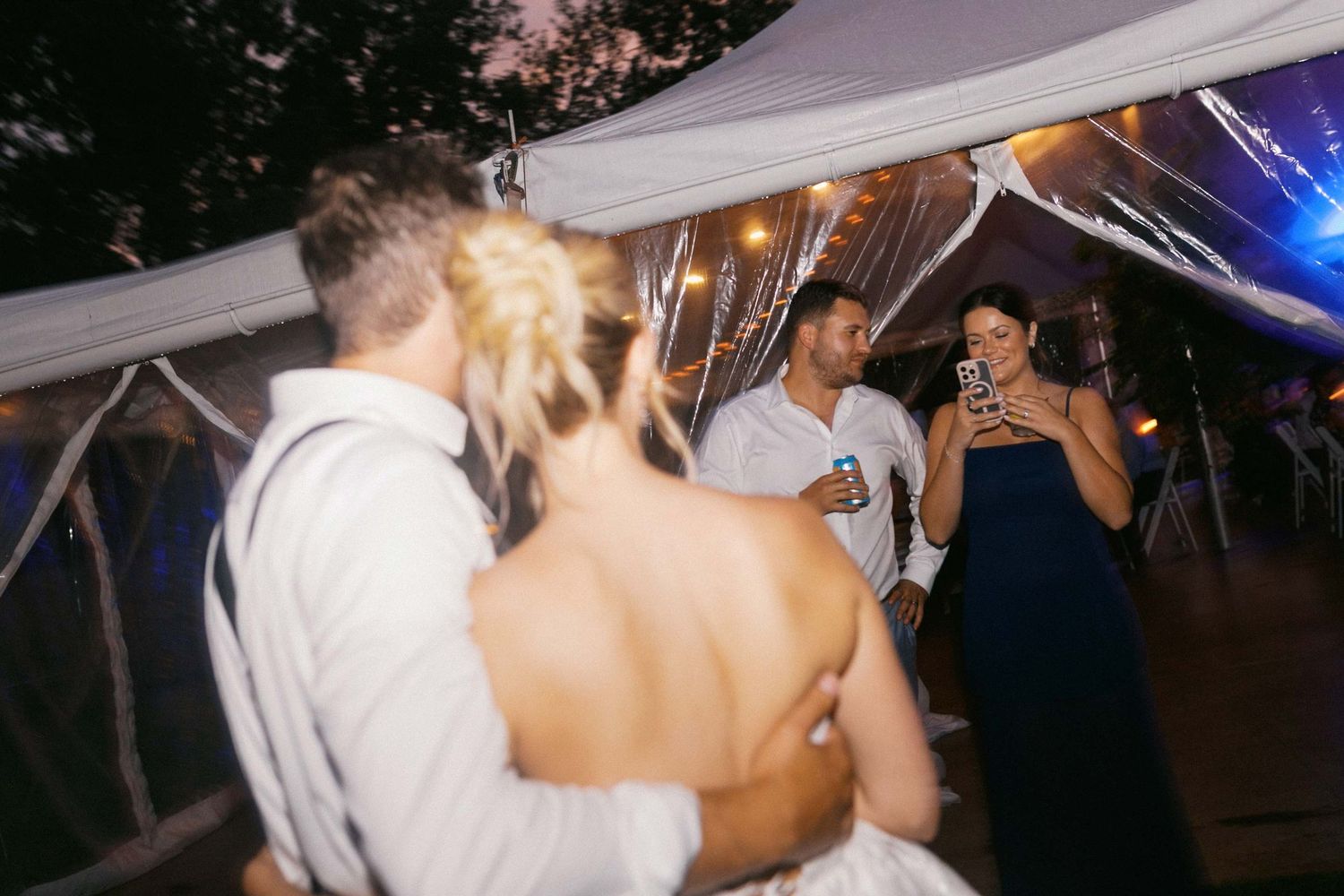 A bride and groom posing together while a guest takes a photo of them during their reception.