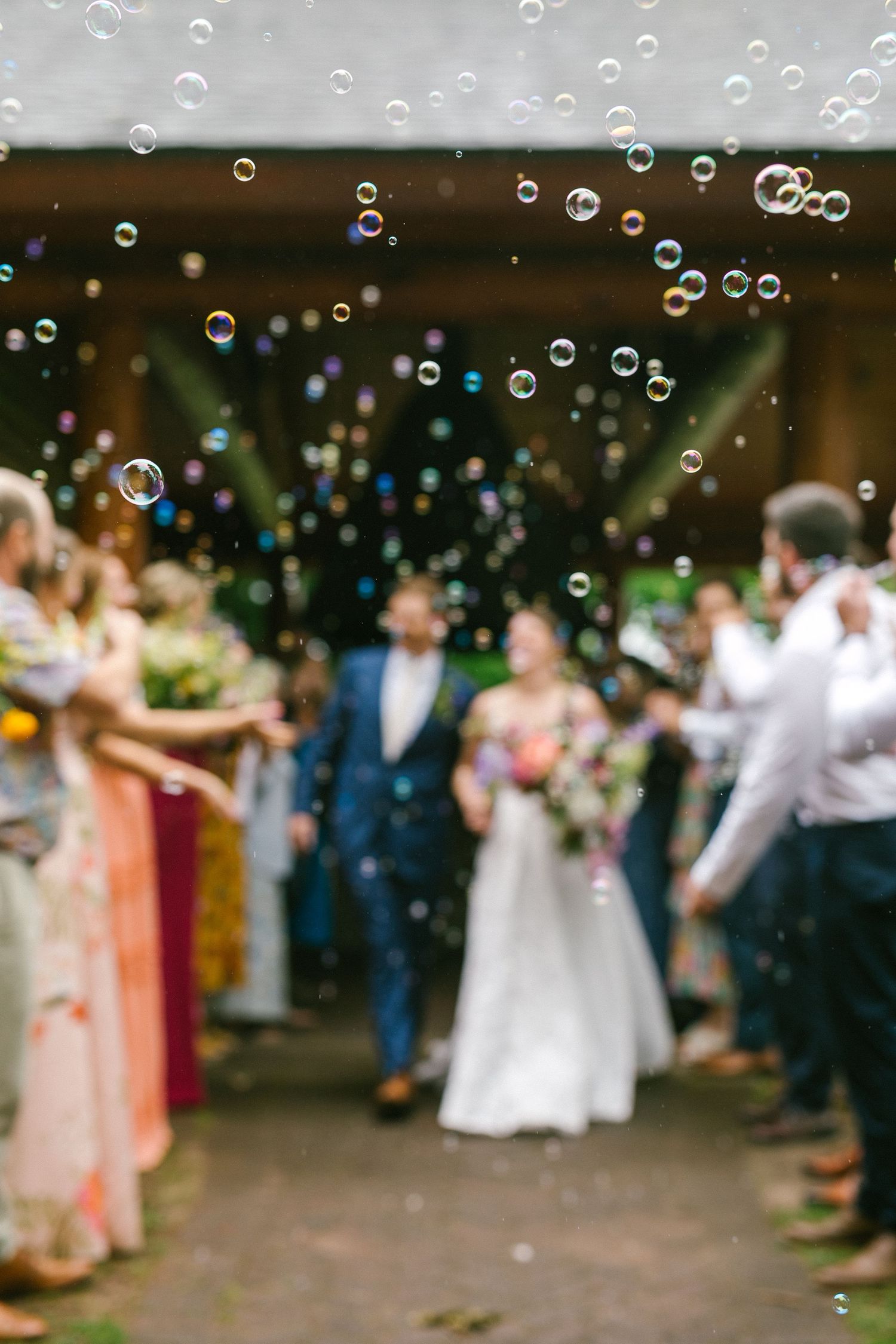 Wedding celebration with soap bubbles floating through the air as guests gather outdoors in formal attire.