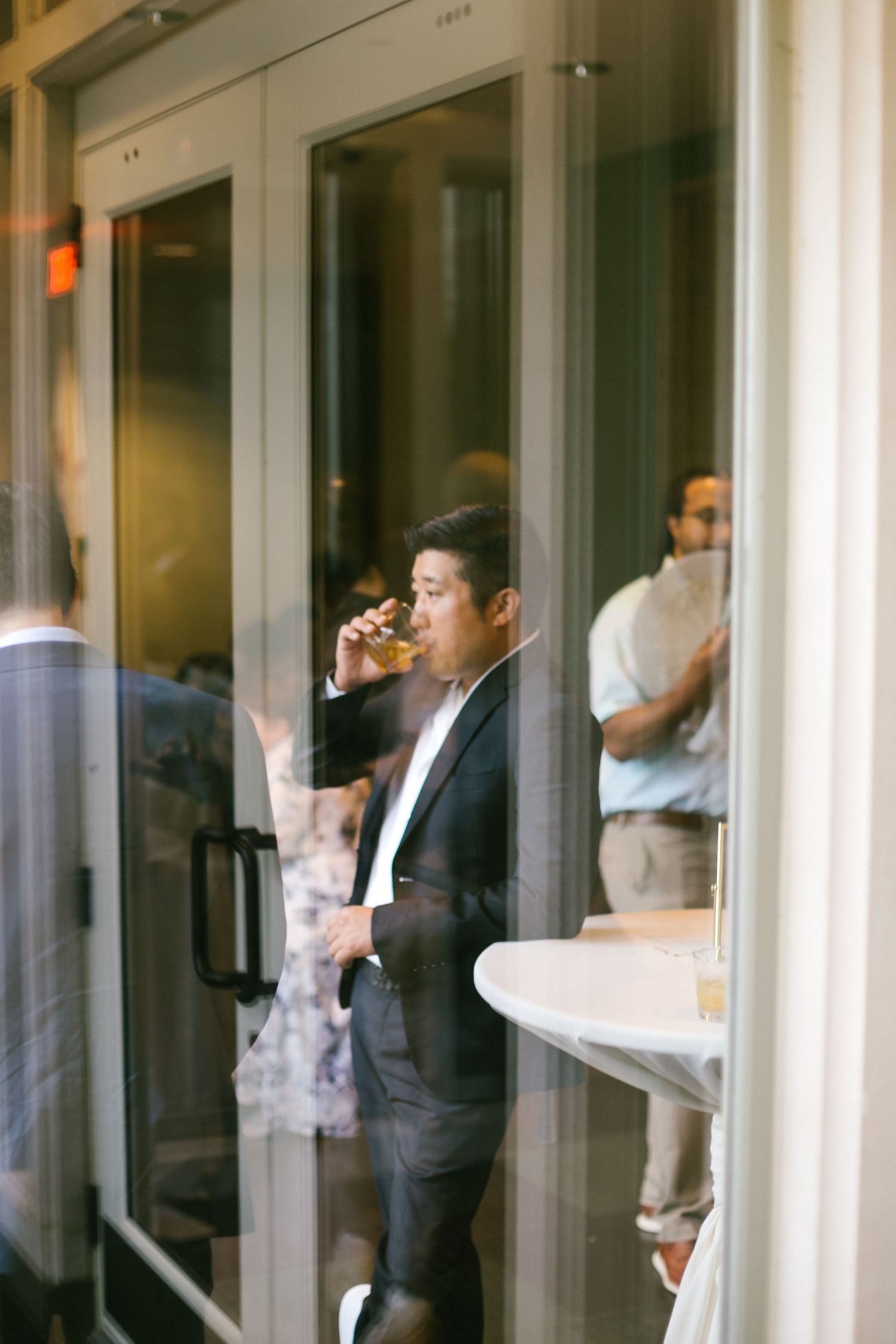 Wedding guest drinking through glass doors at an indoor reception venue.
