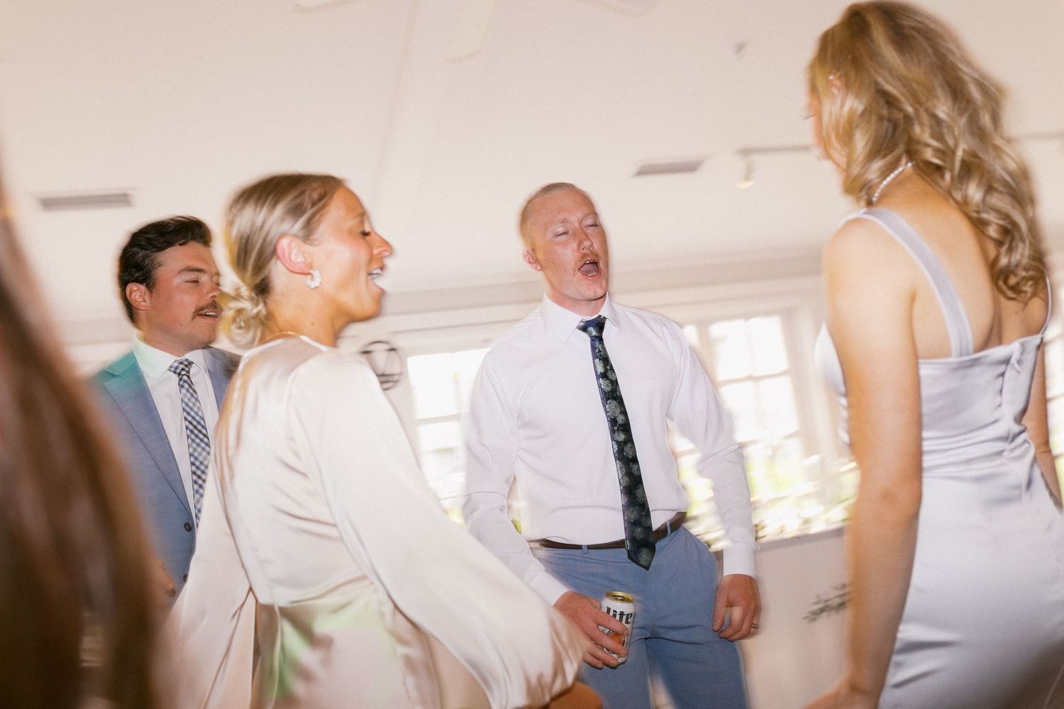 Wedding reception guests dancing and celebrating in a bright indoor venue.