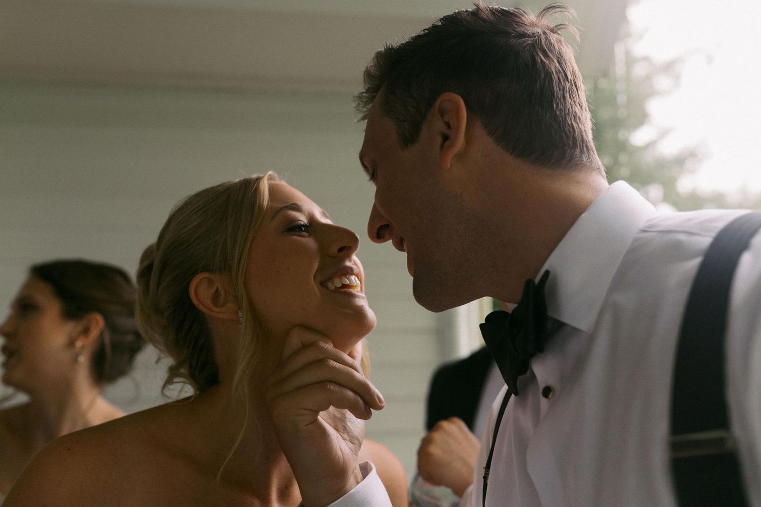 A bride and groom lean in for a kiss while hiding from the rain.