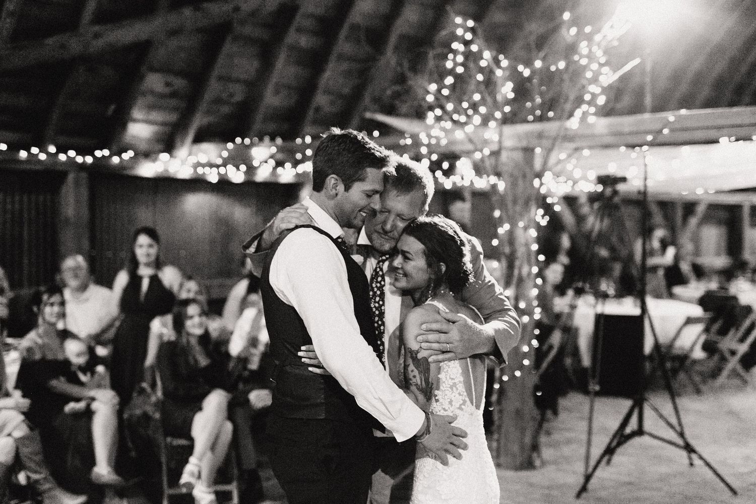 Black and white photo of a couple's first dance at a wedding reception with twinkle lights in the background.