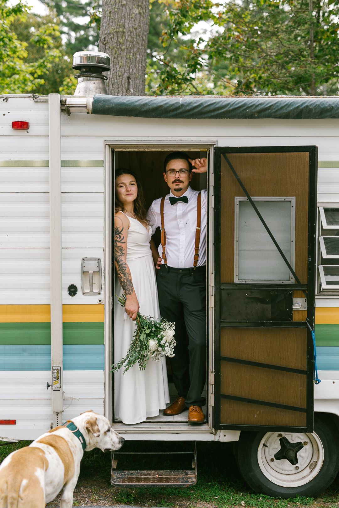 A vintage camper trailer decorated for a wedding with white and green accents.