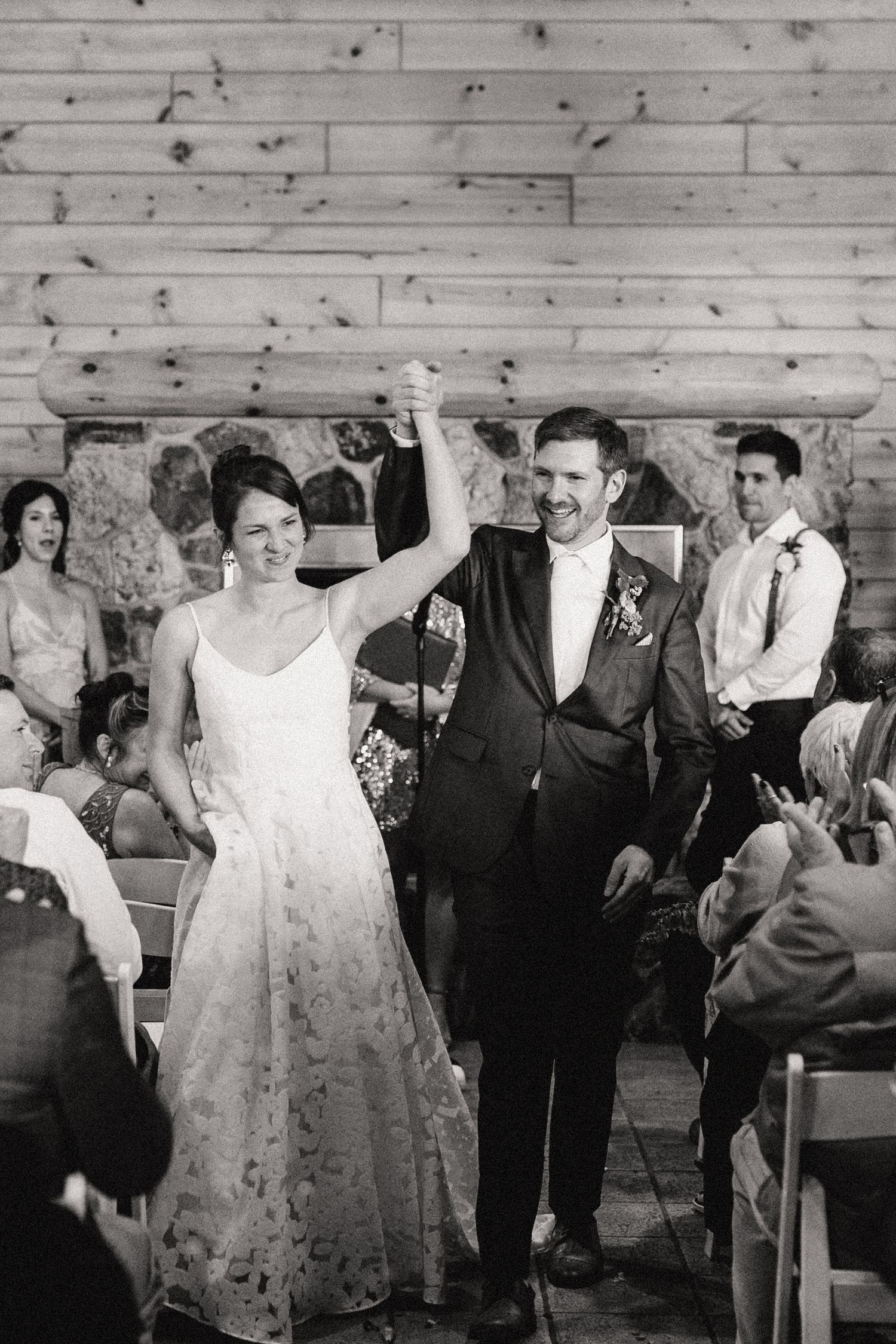 A joyful couple walks down the aisle at their rustic barn wedding celebration in black and white.