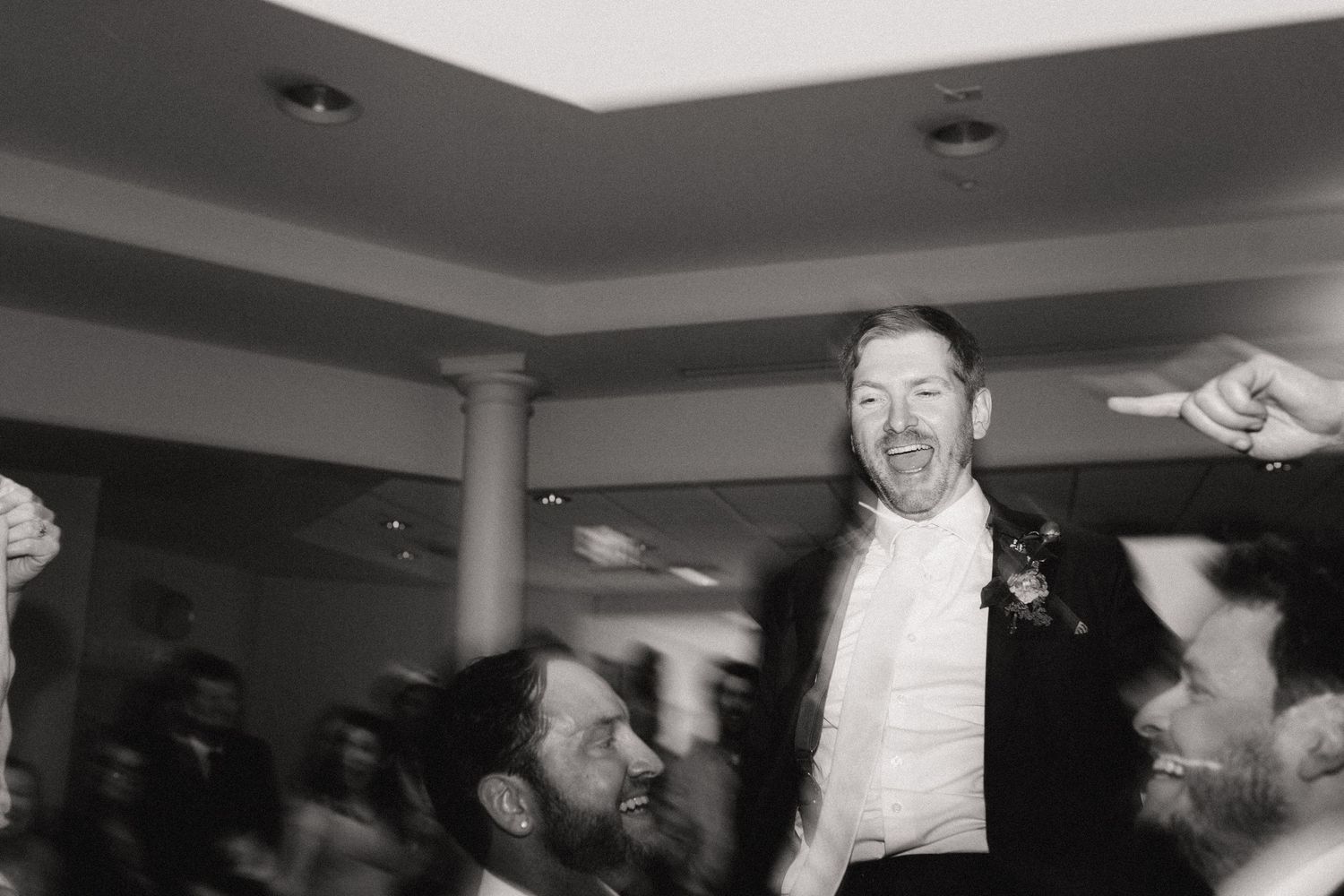 Black and white photo of celebration with person being lifted up by crowd at indoor event.