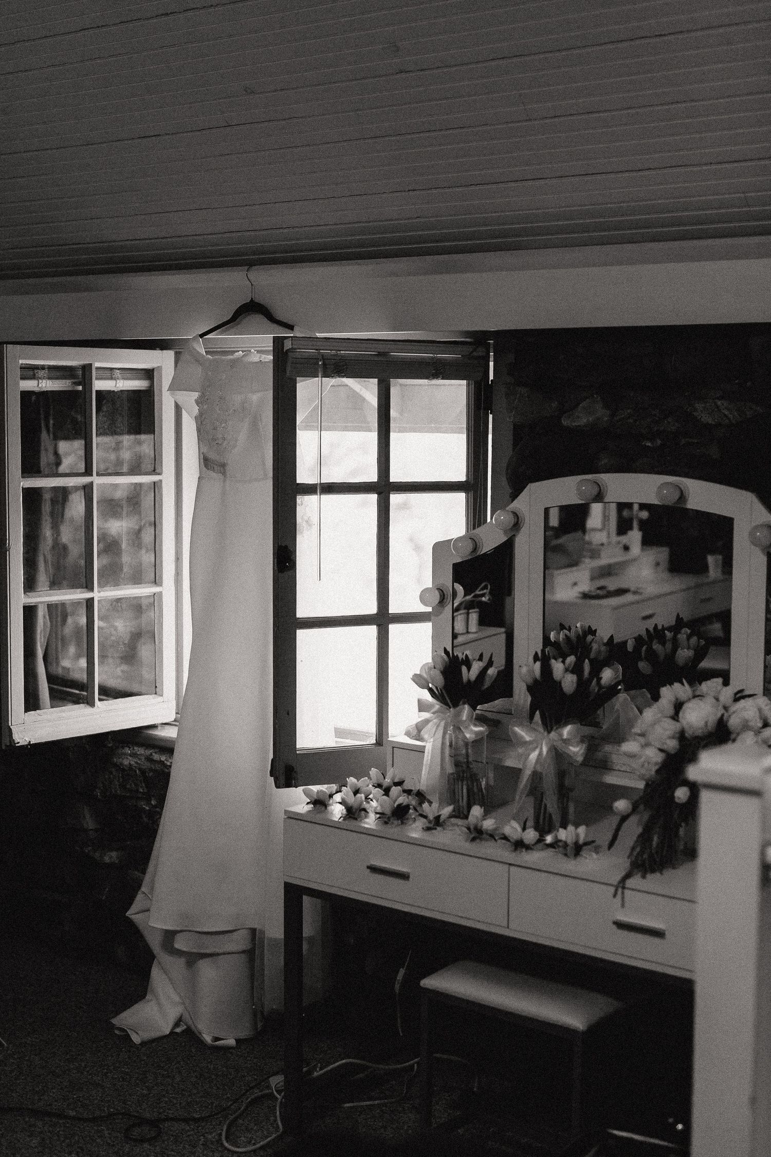 Row of windows in a dark room with white curtains and floral arrangements on the windowsill.