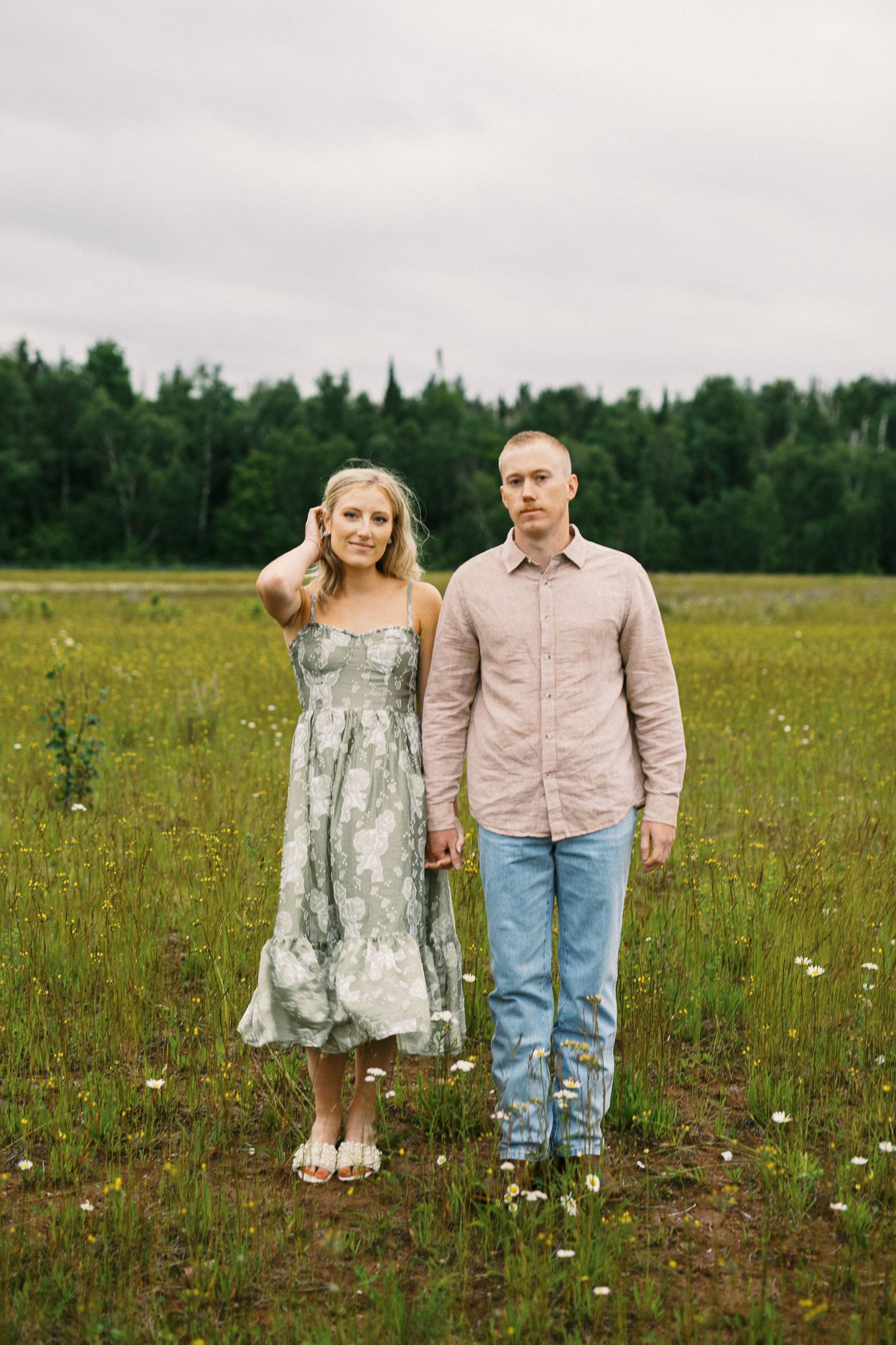 Couple holding hands in a green meadow, woman in floral dress and man in pink shirt and jeans.