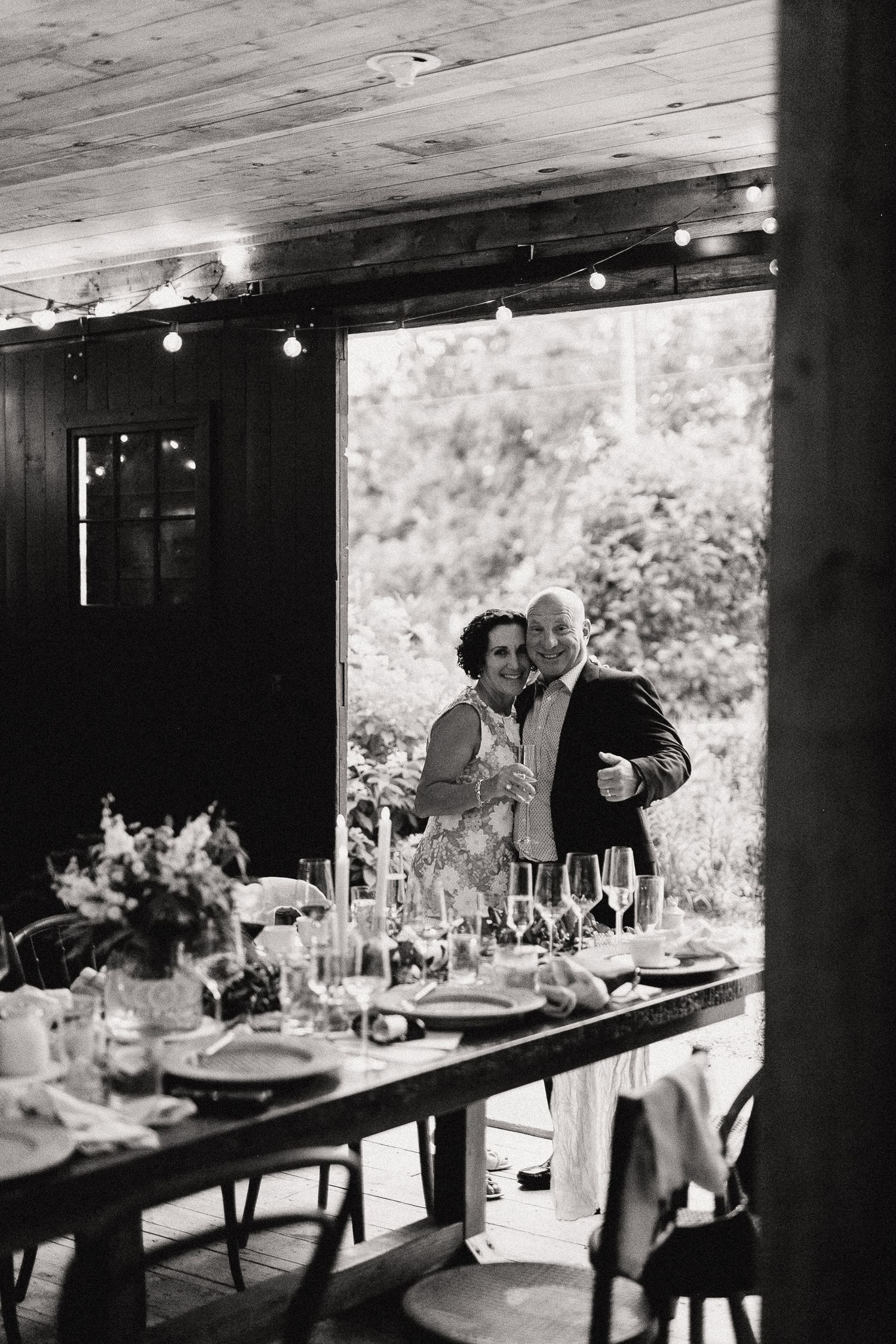 Black and white photo of a couple embracing at an elegantly set wedding reception table with candles and floral arrangements.