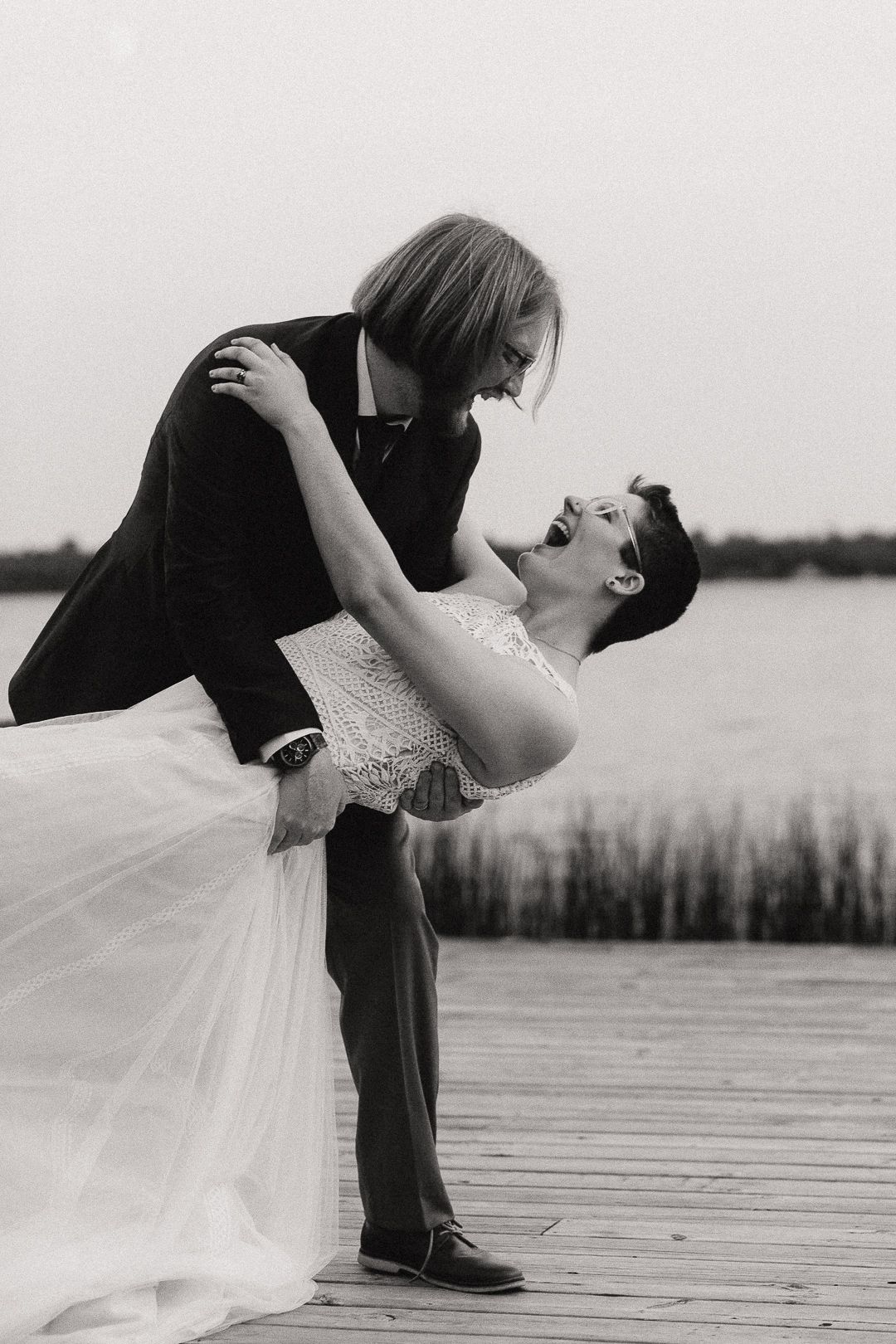A romantic black and white wedding photo sequence showing a dramatic dip pose on a wooden dock by the water.