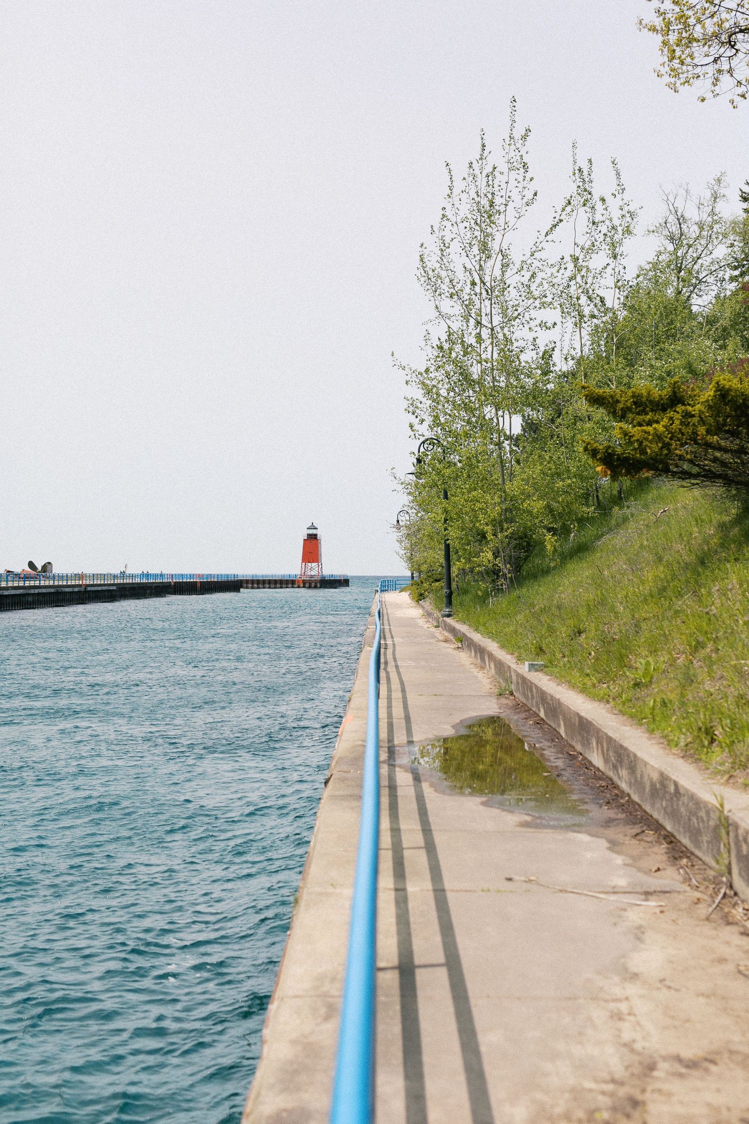 A scenic waterfront path leads to a red lighthouse with trees along the shoreline.