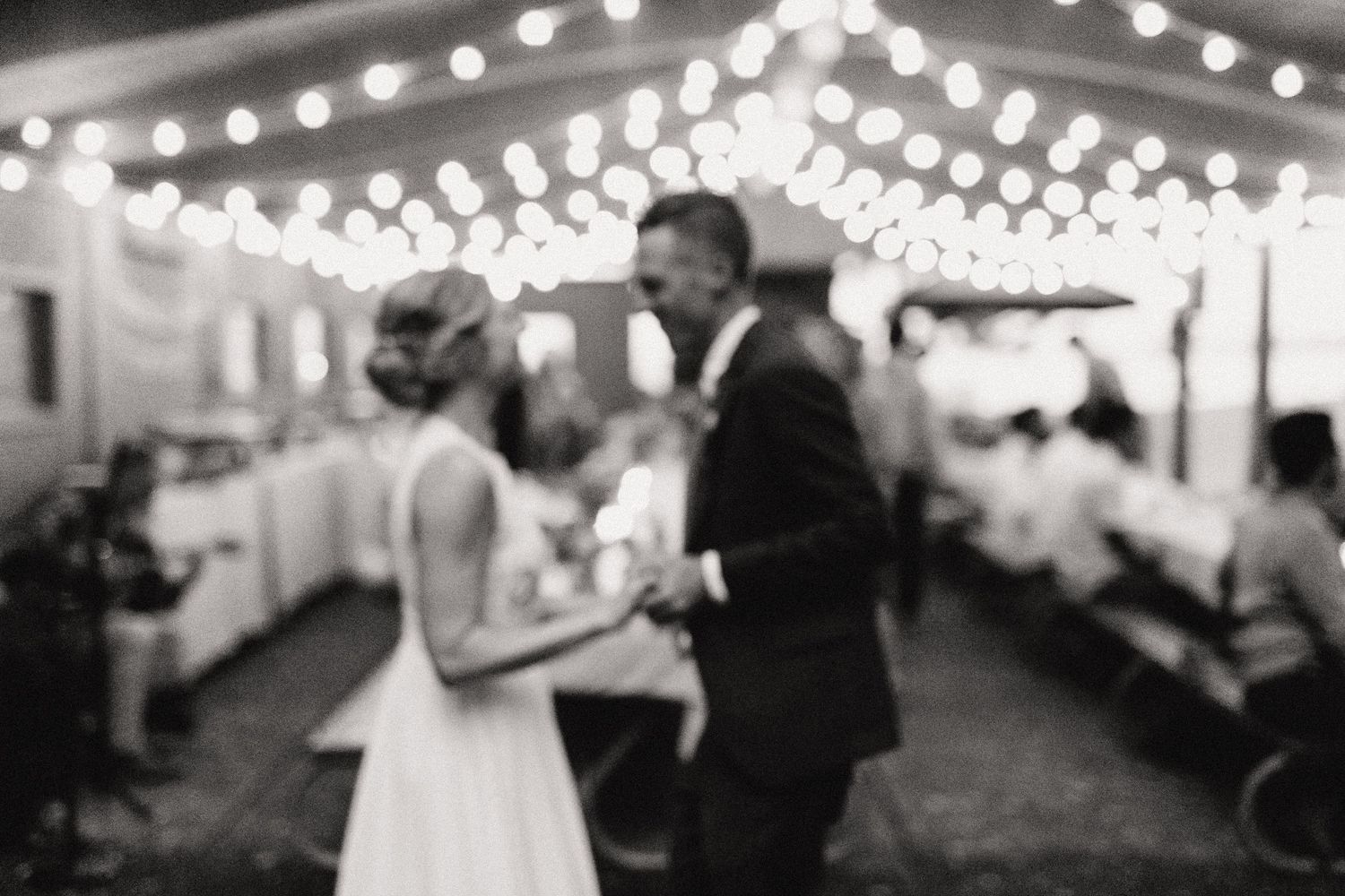 Blurred romantic dance moment at wedding reception under string lights.