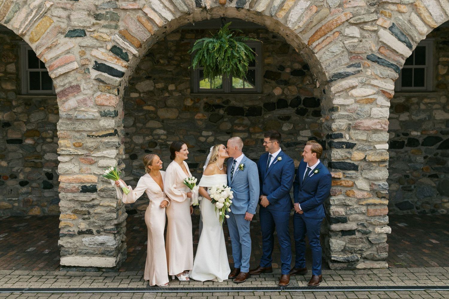 Wedding party poses together under stone archways at an outdoor venue with warm lighting and classic architecture.
