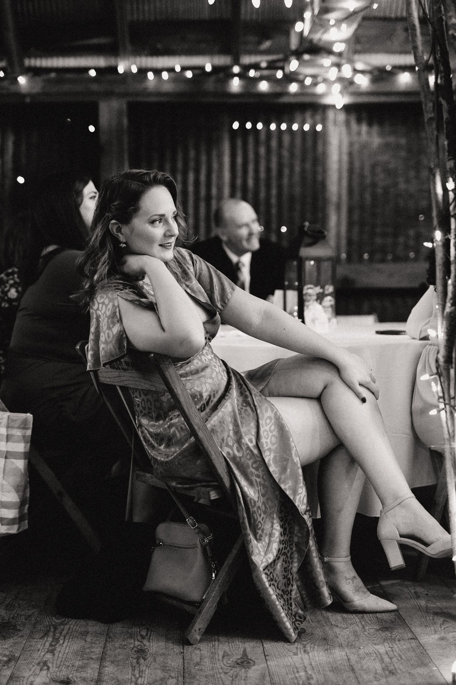 Woman in elegant dress relaxing in chair at dimly lit evening venue.