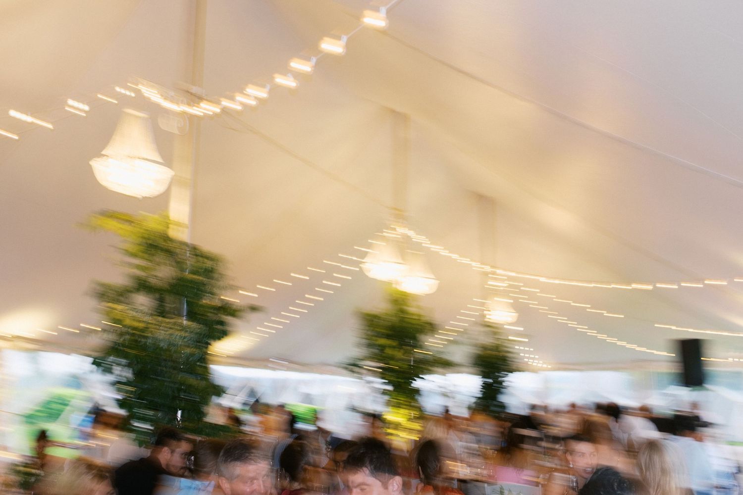 A festive wedding reception venue decorated with string lights and greenery hanging from a white tent ceiling.