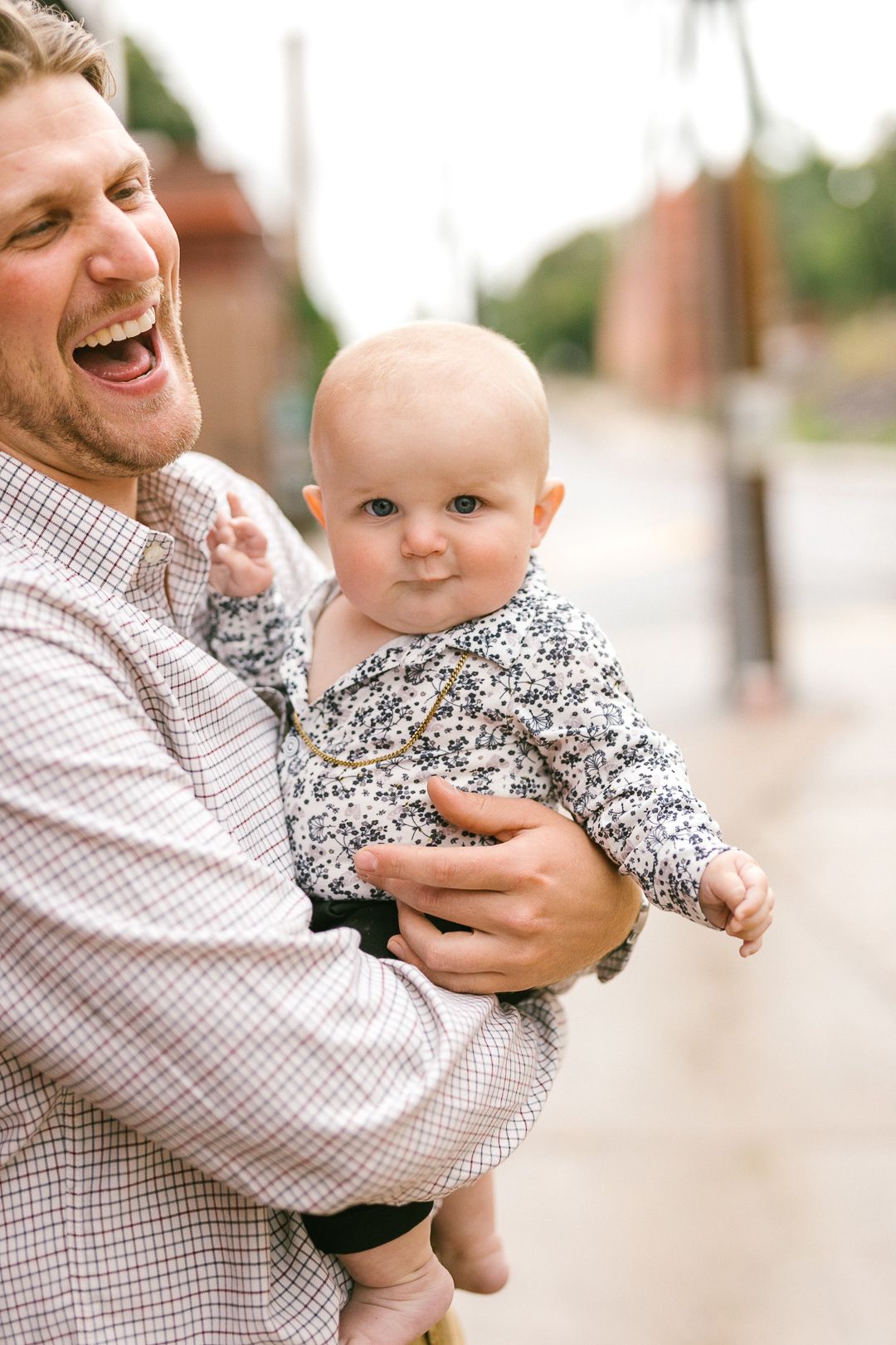 A joyful moment captured between a parent and baby in a floral outfit during a casual outdoor photoshoot.