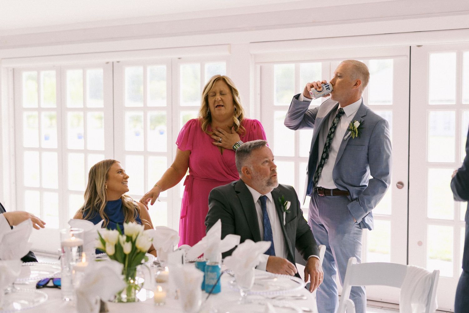 Wedding reception guests mingling in a bright white room with large windows.