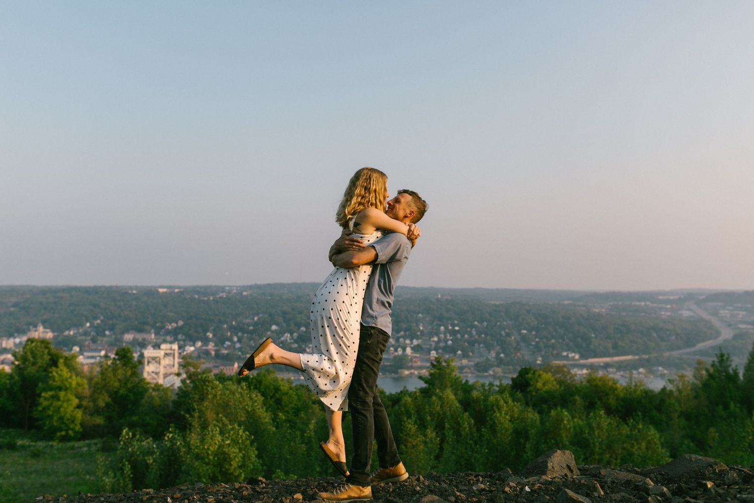 A playful moment captured between a couple on a grassy hilltop with city views.