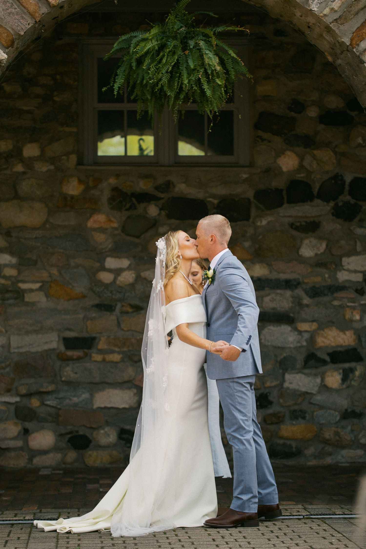 A romantic wedding moment with the couple kissing against a rustic stone wall backdrop.