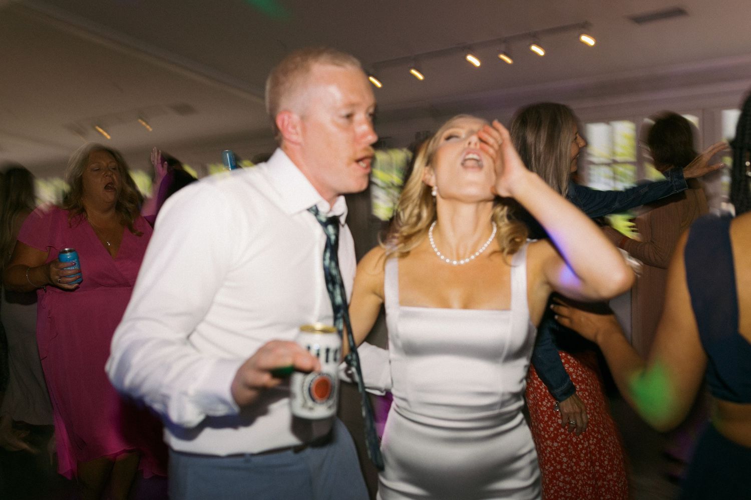 People dancing and having fun at a wedding reception event in an indoor venue with colorful lighting.