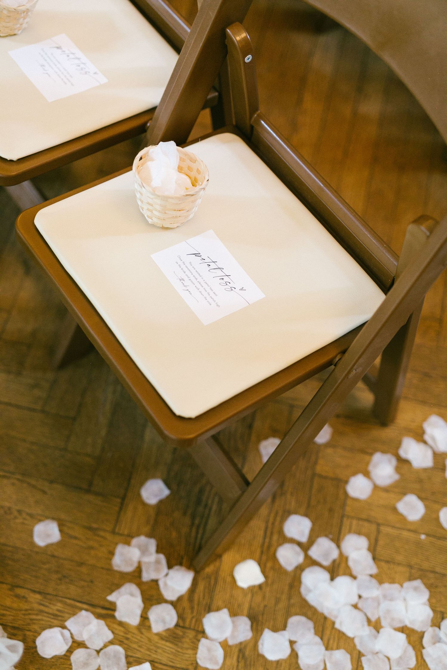 Wedding ceremony chairs with programs and flower petal basket on hardwood floor.