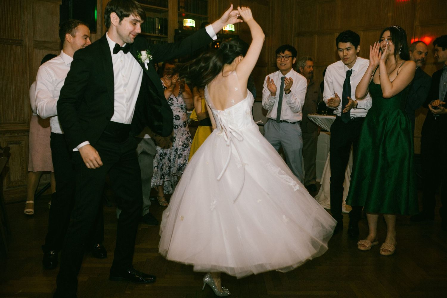 Bride and groom dancing at wedding reception while guests clap and celebrate in elegant venue.