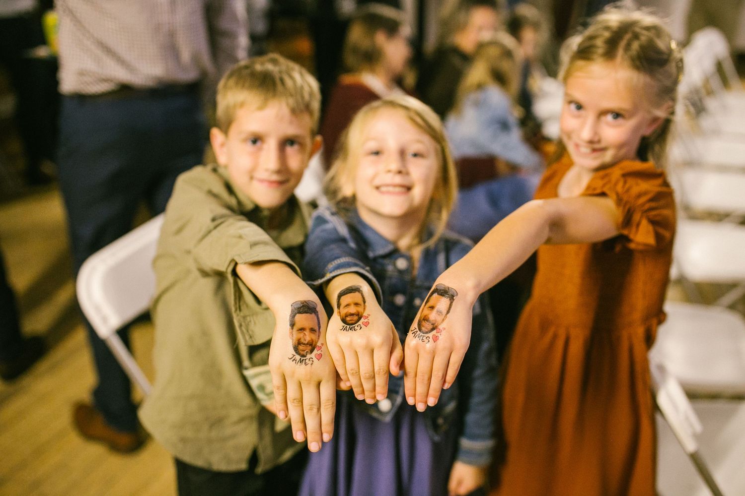 Three children showing off temporary tattoo designs on their hands at an event.