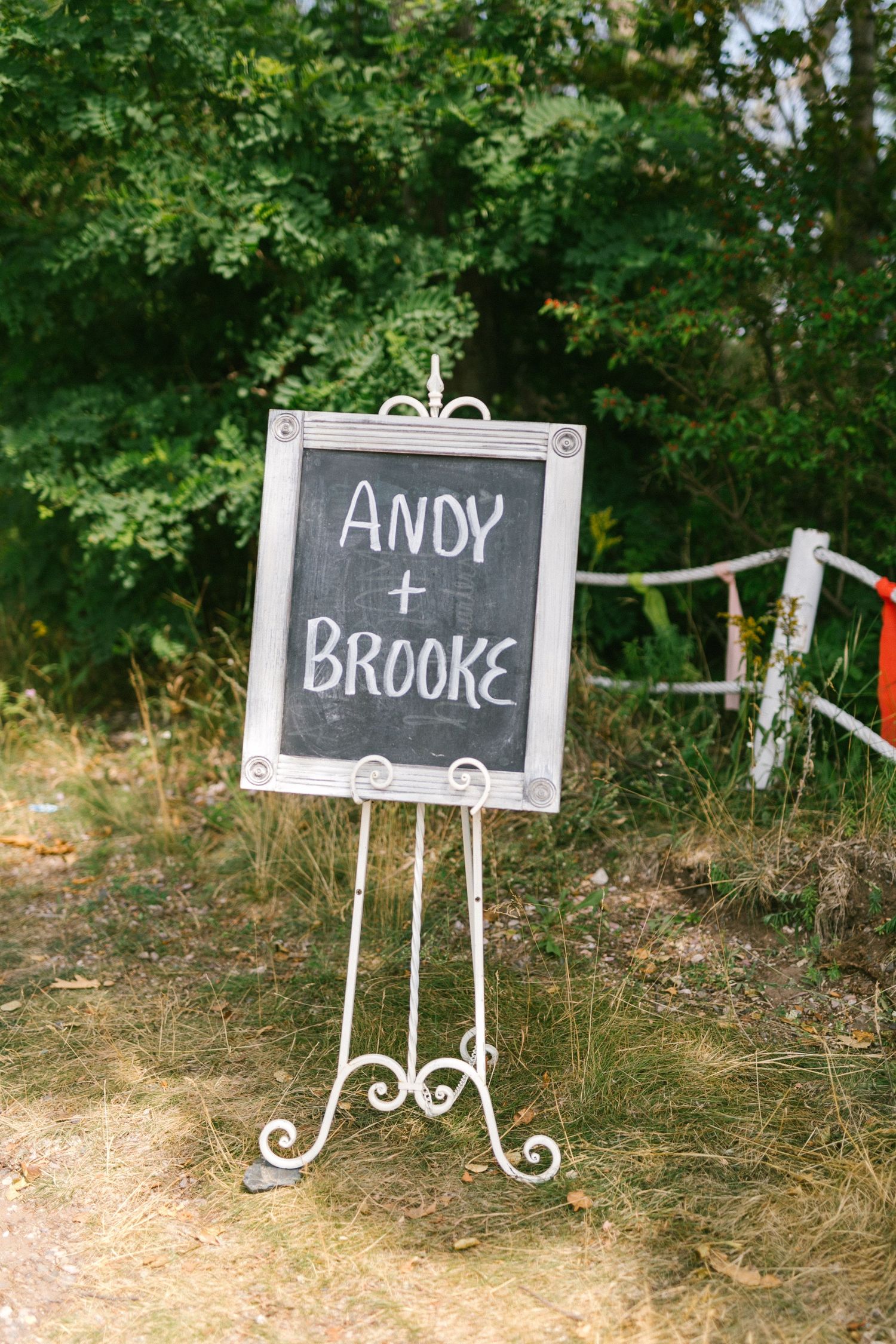A series of decorative chalkboard signs on white metal stands displayed outdoors against a natural green backdrop.
