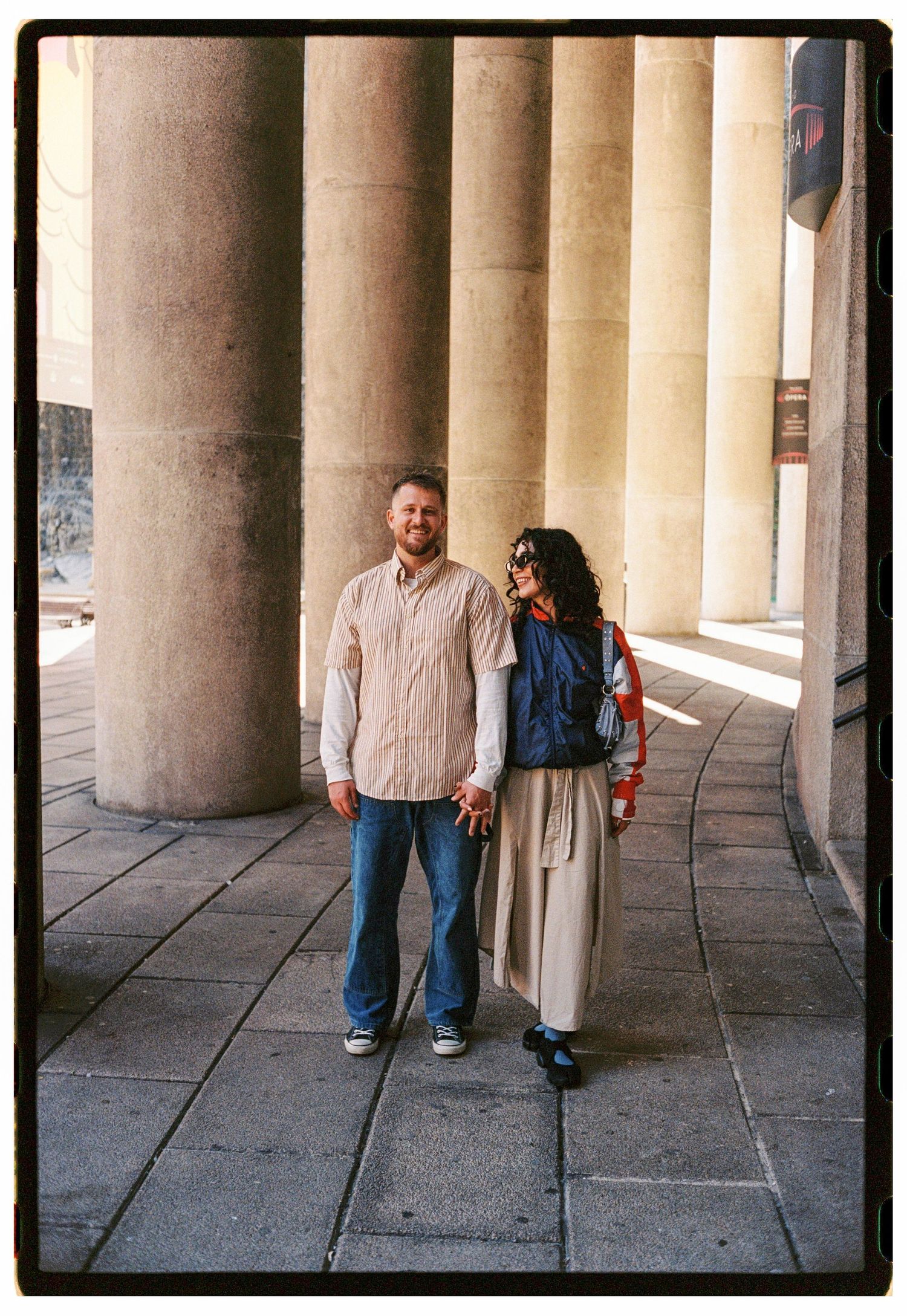 Couple standing together among grand stone columns at a classical architectural landmark.