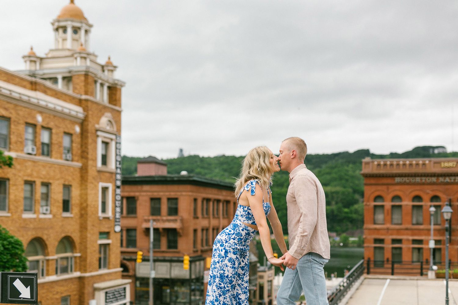 Couple almost kissing on rooftop with historic brick buildings in background.