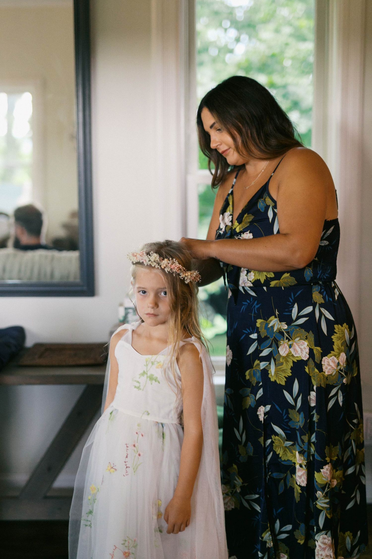 A tender moment shared between a mother in a floral dress and a flower girl in a white dress during a wedding.
