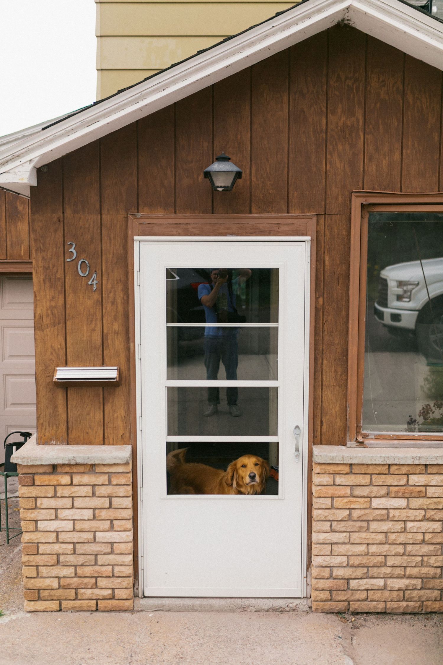 Golden retriever dog peering through glass storm door of brown wooden house number 304.