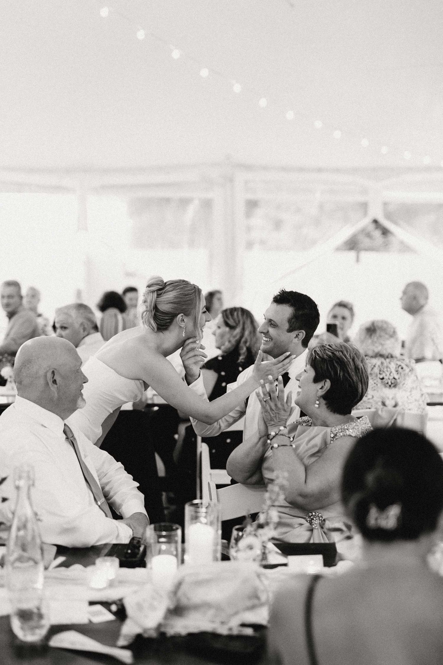 Black and white photo of wedding reception guests seated at tables engaged in lively conversation during dinner.