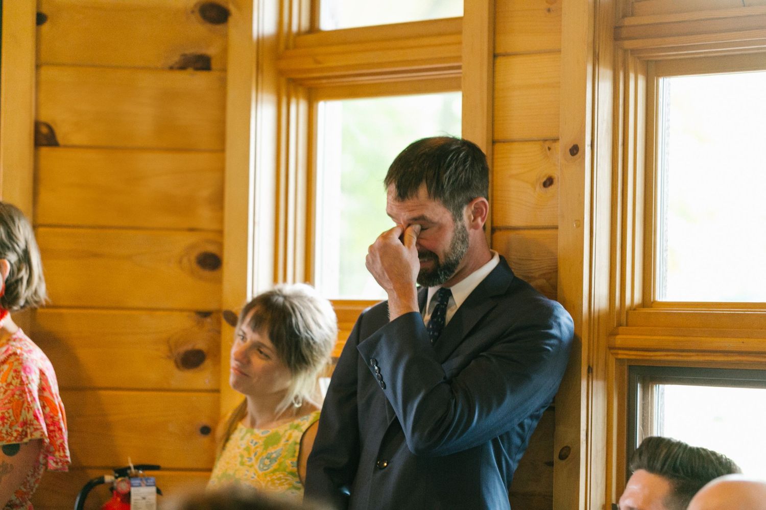 People gathered indoors in a wood-paneled room with windows in a candid moment during an event.