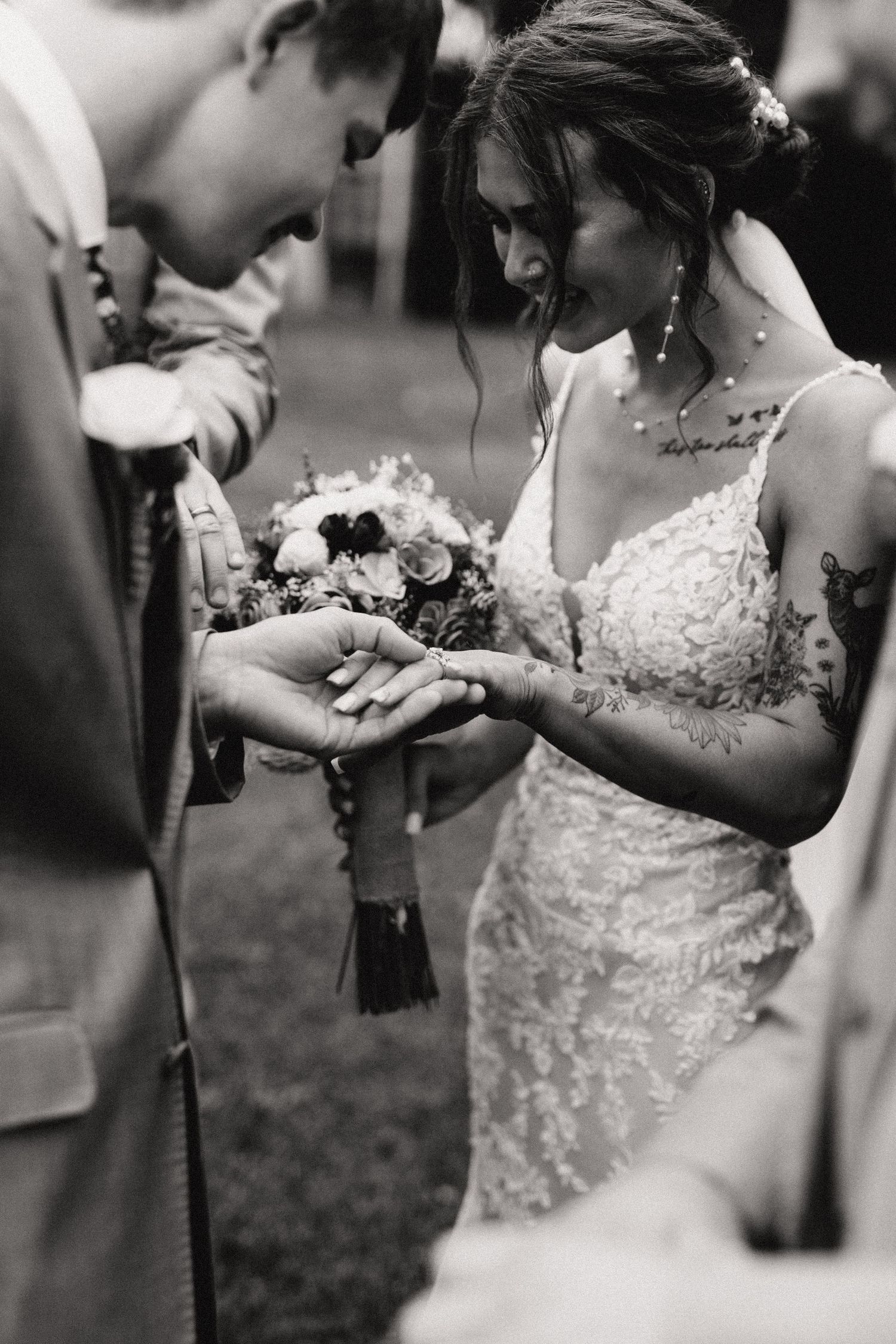 A heartfelt black and white wedding moment as the bride and groom exchange rings while holding a floral bouquet.