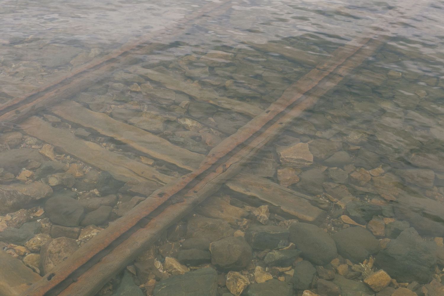 Aerial view of railroad tracks crossing through rocky terrain seen through clear water.