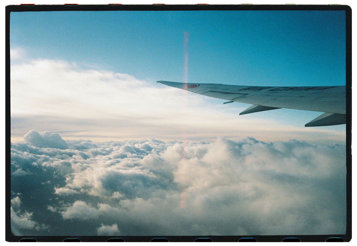 View of airplane wing above fluffy white clouds from passenger window seat.