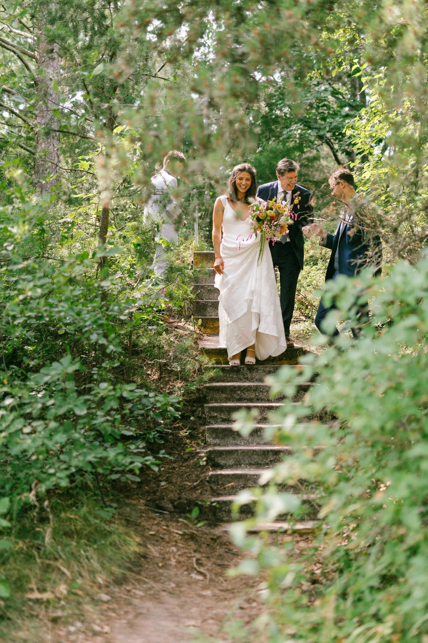 Wedding party walks down rustic stone steps surrounded by lush greenery in a garden setting.
