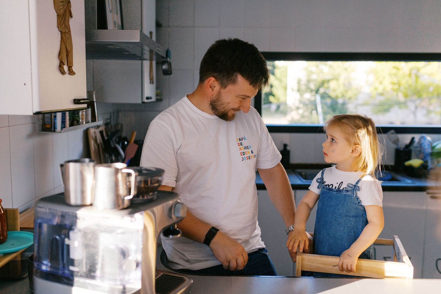 Father and young daughter cooking together in a modern kitchen with a rolling pin.