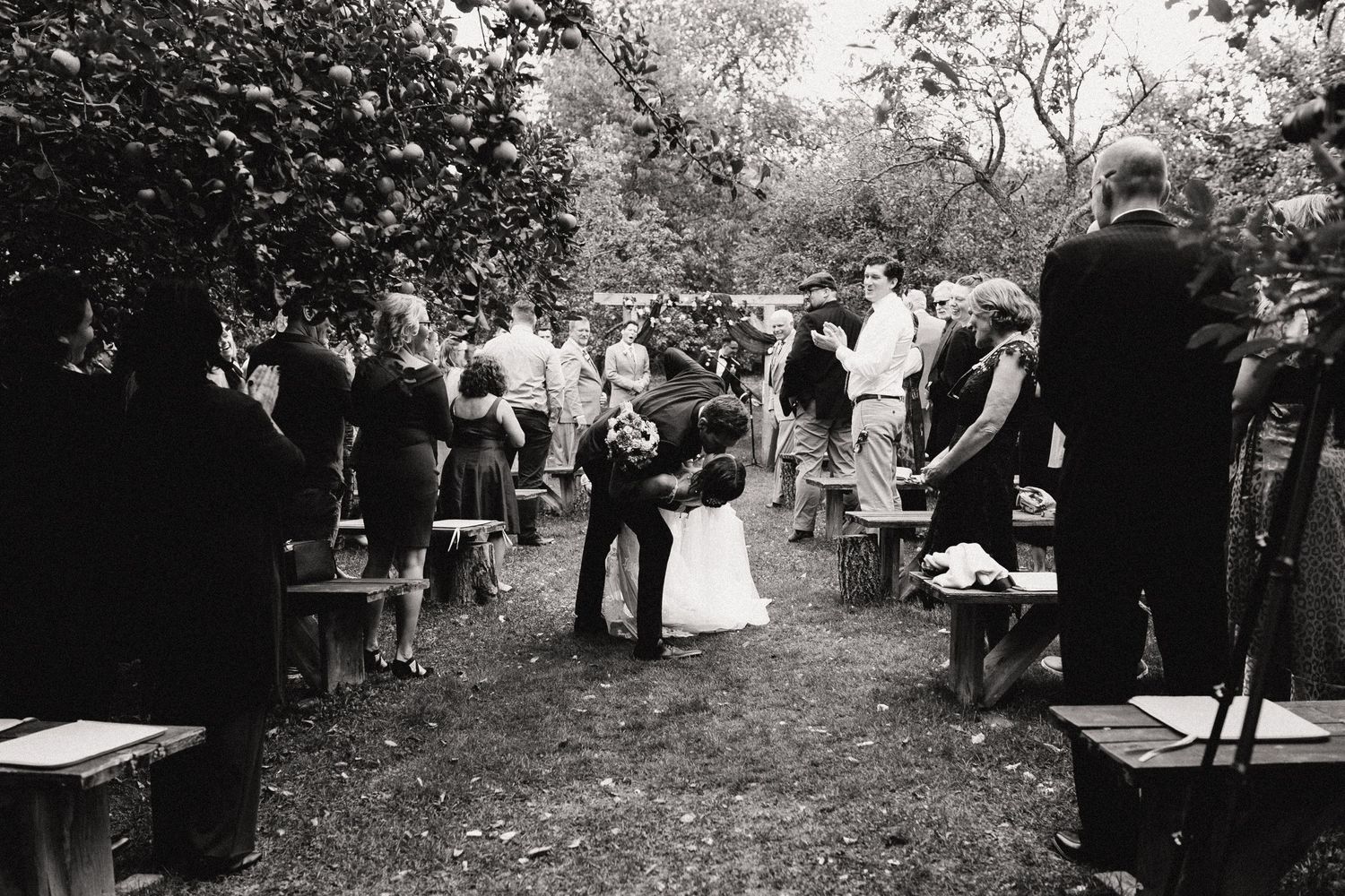 Black and white photo of an outdoor wedding ceremony with guests standing along a garden path.
