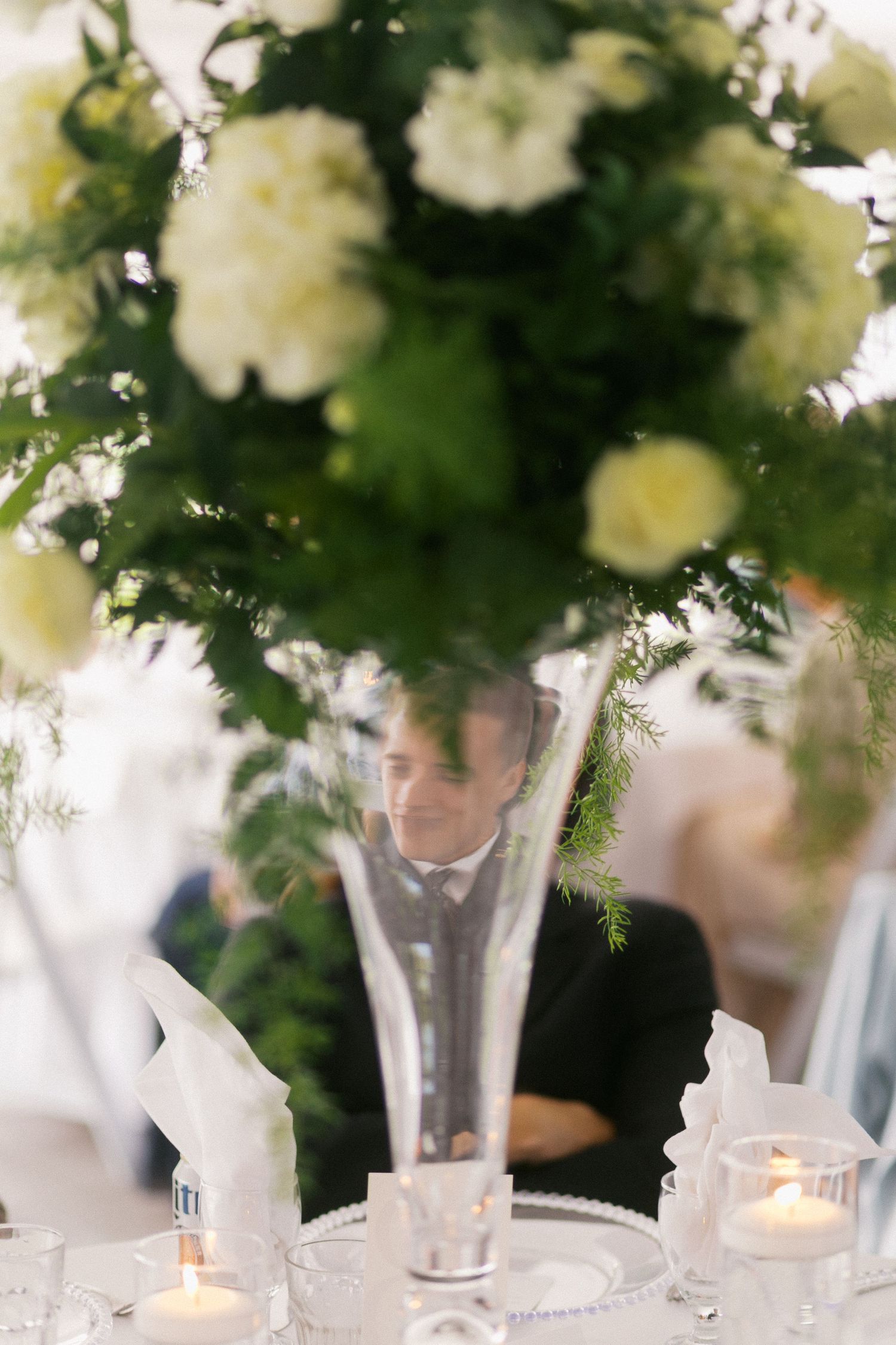 White floral centerpieces in glass vases line an elegant table setting with glowing candles.