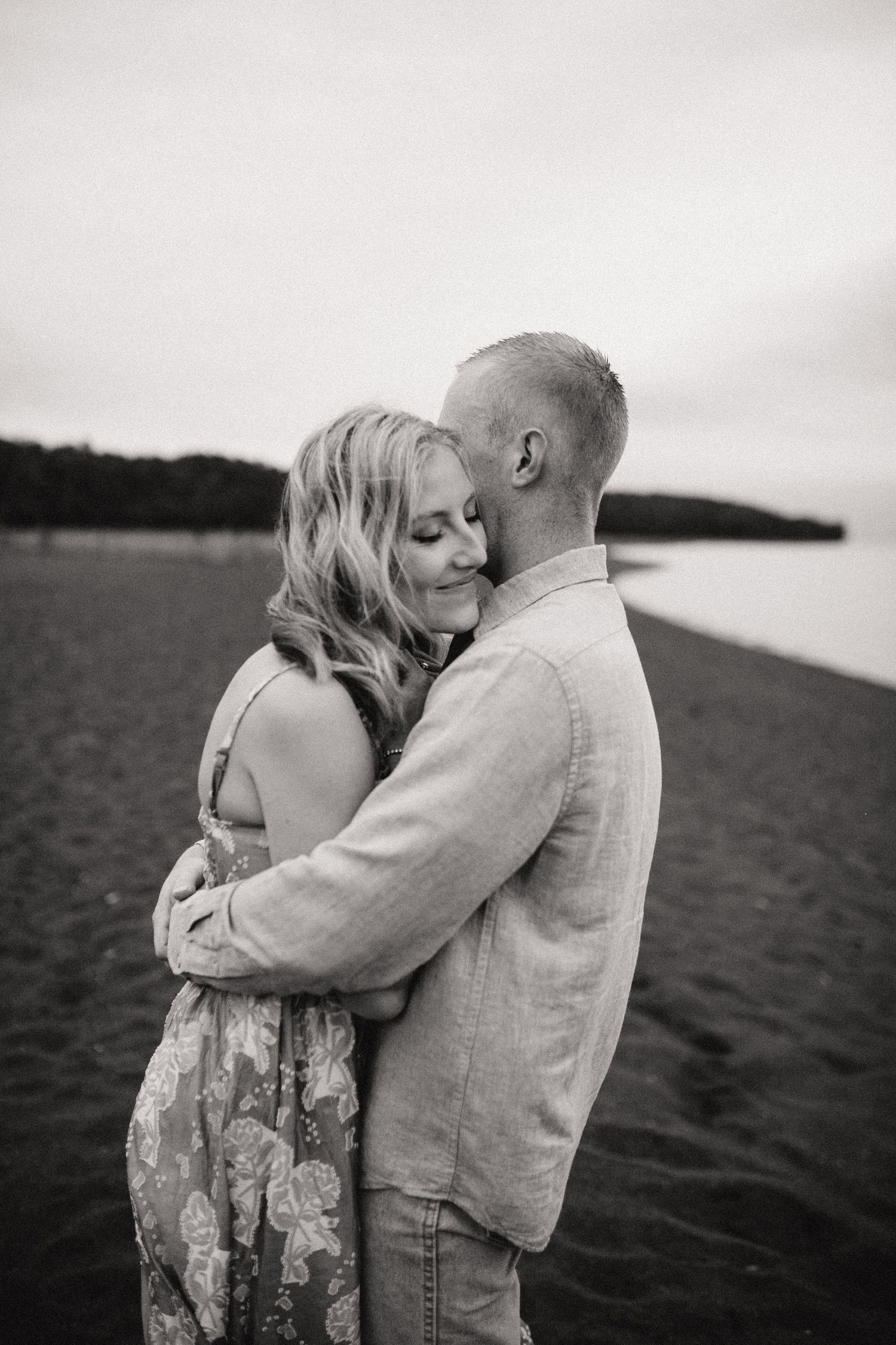 Intimate embrace between couple on beach with moody overcast sky.