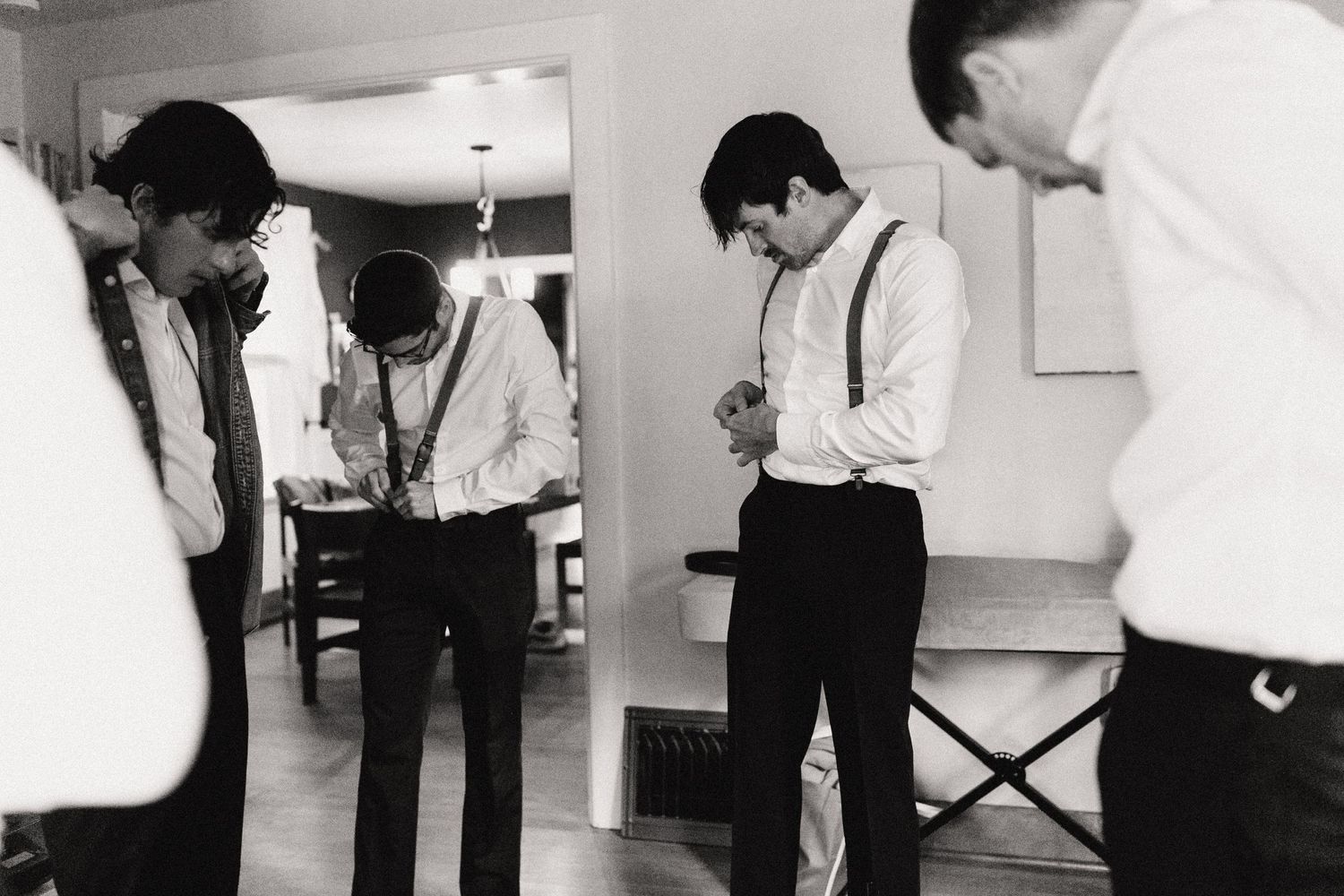 Several people in formal attire stand preparing in a hallway, captured in black and white photography.