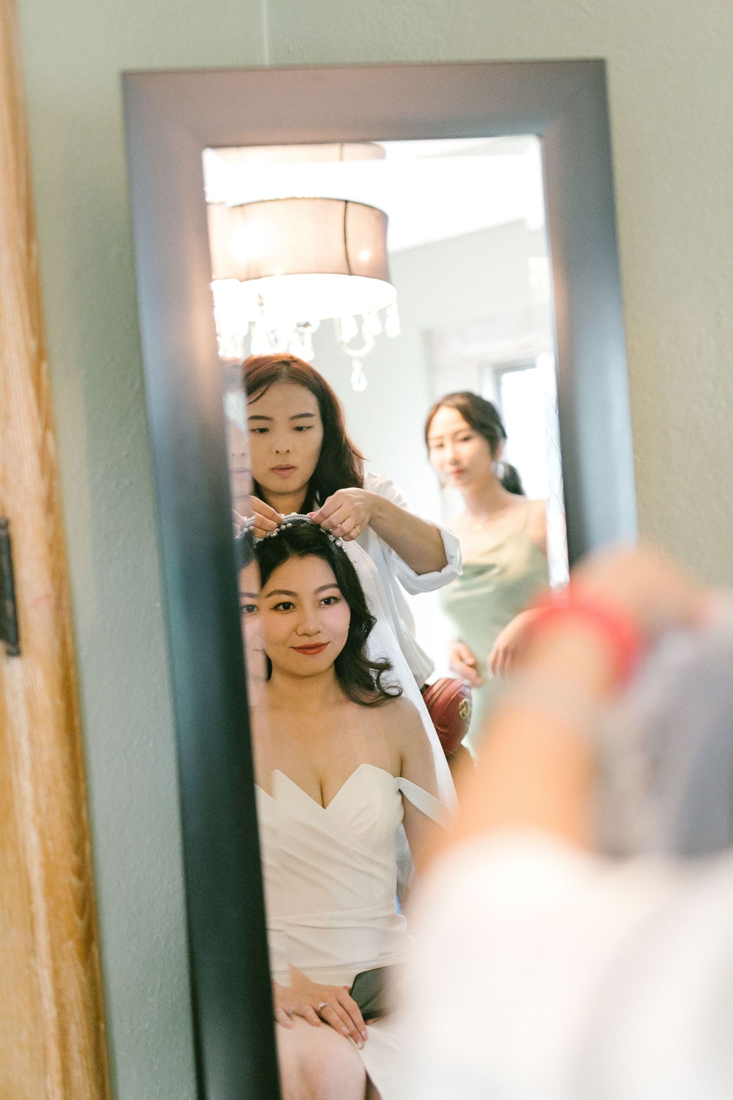 Bride getting hair done by stylists reflected in a large mirror during wedding day preparations.